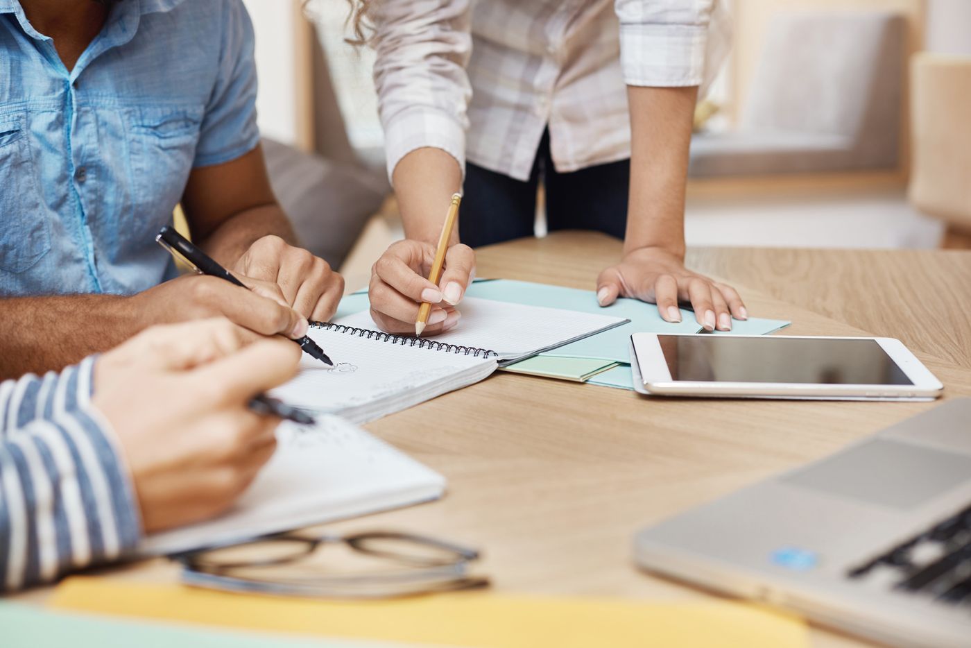 Tres personas anotando en cuadernos sobre una mesa de madera, con una tablet y una notebook al costado
