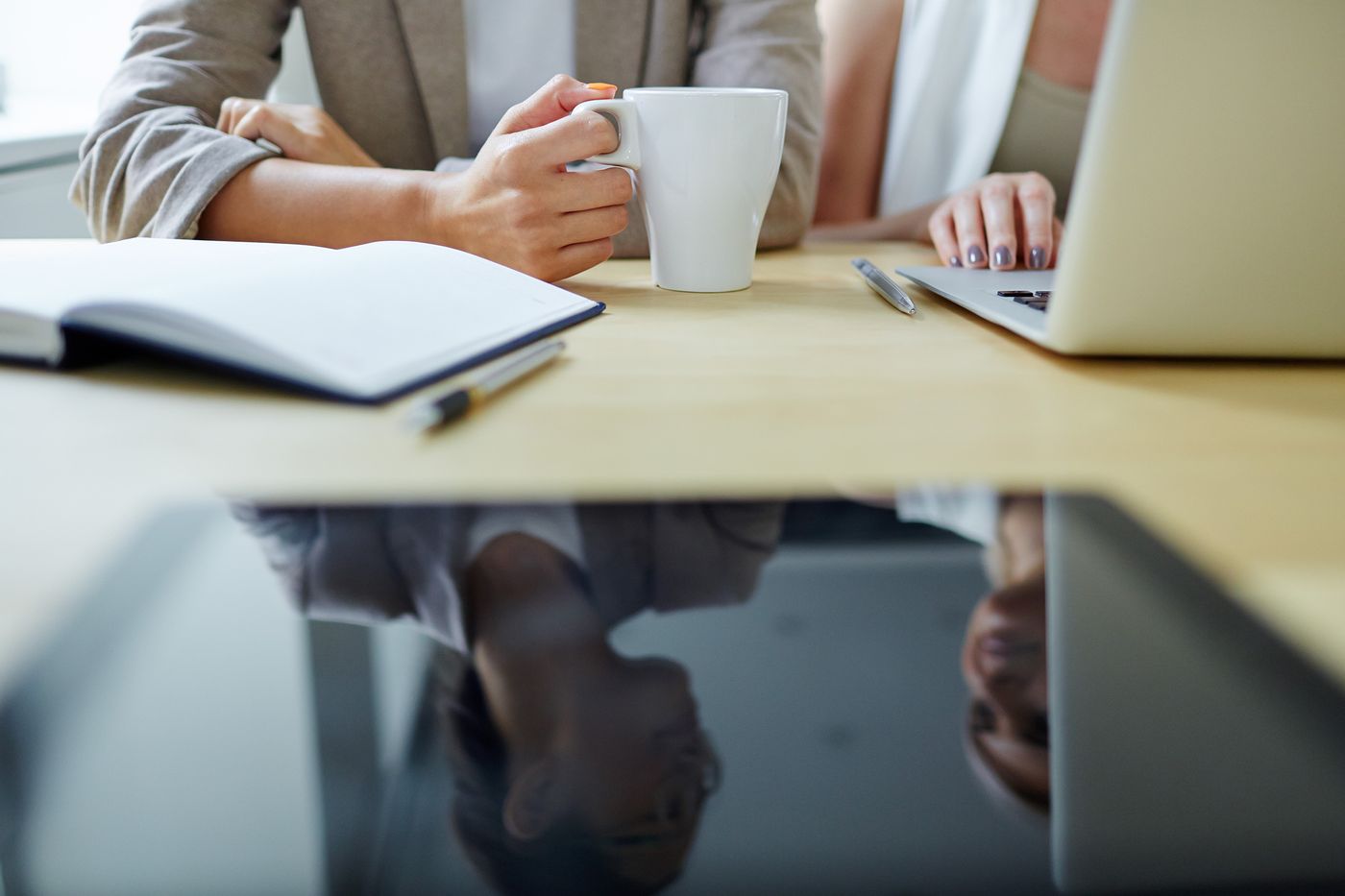 Dos personas sentadas a una mesa de madera clara, con una taza blanca, una libreta abierta y una notebook